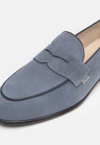 Mocassino in suede blu con punta arrotondata, dettagli decorativi in cuciture e una fodera in pelle liscia. Presenta un design minimalista e una suola in gomma.