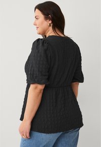 Zwarte blouse met textuur, met pofmouwen, een getailleerde taille en een relaxte pasvorm. De stof heeft een geruit patroon.