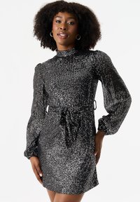 Black sequined dress with a high neckline, long puff sleeves, and a tie belt at the waist. Features shimmering texture and short length.