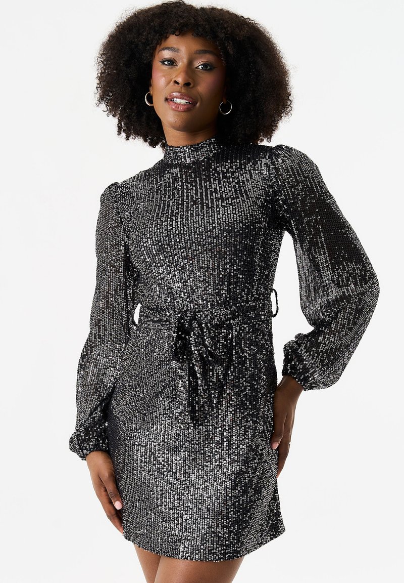 Black sequined dress with a high neckline, long puff sleeves, and a tie belt at the waist. Features shimmering texture and short length.