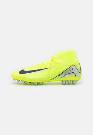 Jasnożółty korki Nike z czarnym znakiem, kołnierzem wokół kostki i srebrnymi korkami zapewniającymi przyczepność na twardym podłożu, pokazany z boku na białym tle.