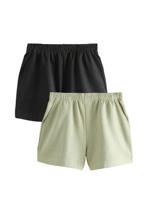 Mladá žena s čiernymi vlasmi v drdole má na sebe sivý tielkový top, čierne šortky a čierny popruh cez telo, pozerá nadol.