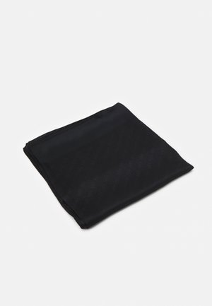 Foldet sort stofkvadrat med glat tekstur, hvilende på en hvid overflade med svage skygger.