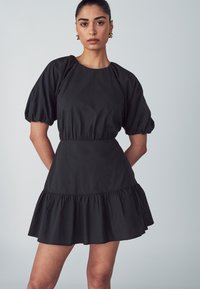 Czarna sukienka z krótkimi puff sleeves, dopasowanym gorsetem i falbaniastym dołem. Wykonana z gładkiego materiału, z prostym okrągłym dekoltem.