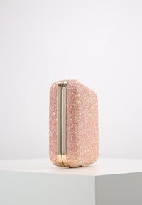 Pochette rigide rose avec texture en paillettes fines. Présente des accessoires en métal doré et une forme rectangulaire aux bords arrondis.