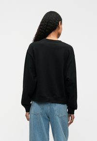 Svart hettegenser med avslappet passform, rund hals og lange ermer. Kombinert med lyseblå avsmalnende jeans, med standard sømmer og lommer.