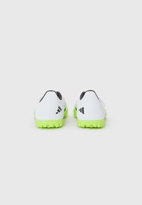 Zapatos deportivos blancos con suela de goma verde, con acentos negros en el talón y el logo. Material suave, diseño de corte bajo.