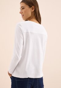 White long-sleeve T-shirt featuring a round neck, soft cotton material, and a back seam detail, paired with dark denim jeans.