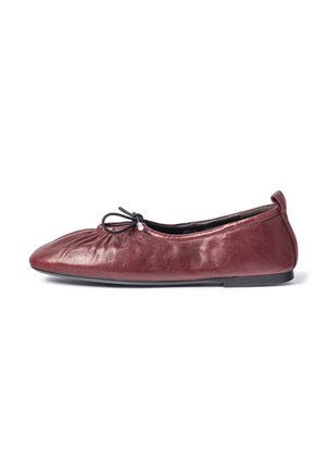 Chaussure de ballet plate en cuir bordeaux avec l’avant froncé et un petit nœud noir sur une fine semelle noire, vue de côté.