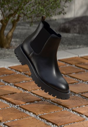Bottine Chelsea en cuir noir avec un panneau latéral élastique en relief et une semelle en caoutchouc texturé. Design élévé avec une finition lisse.