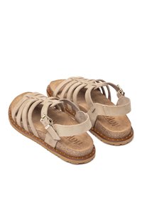 Beige Wildledersandalen mit mehreren Riemen, verstellbarem Knöchelverschluss, strukturiertem Fußbett und brauner Gummisohle mit kleinen Noppen für besseren Halt.