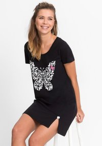 Abito nero a maniche corte con un design di farfalle bianche e rosa, fessure laterali con accenti a forma di cuore bianchi e una vestibilità rilassata.