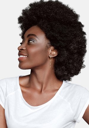 Orecchini d'oro pendenti con un design geometrico, indossati da una persona con capelli neri e texturizzati, in una t-shirt bianca su uno sfondo neutro.