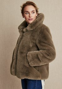 Brun faux fur-jacka med hög krage, sidfickor och en mjuk struktur. Har en boxig silhuett och en dold framknäppning.