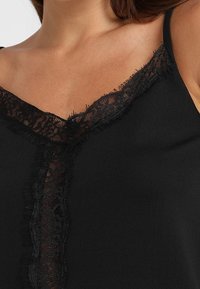 Camisole noire avec un décolleté en V orné d'une délicate bordure en dentelle noire et des bords effilochés, fabriquée en tissu doux et léger.