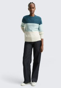 Pull en maille avec un col rond dégradé bleu-vert, associé à un jean large bleu foncé et des baskets blanches. Texture lisse, coupe décontractée.
