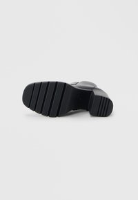 Bottes en cuir noir avec une semelle texturée, comportant des rainures horizontales pour l'adhérence. Pas de logos visibles ni d'éléments décoratifs supplémentaires.