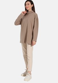 Beige t-shirt met lange mouwen en hoge kraag, gecombineerd met lichtbeige slim-fit broek en witte sneakers, met een relaxte pasvorm en zachte textuur.
