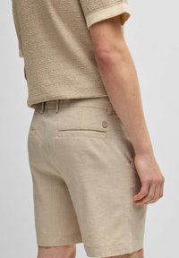Pantaloni corti beige in lino con una finitura texture, dotati di due tasche posteriori e un dettaglio logo vicino alla tasca destra.