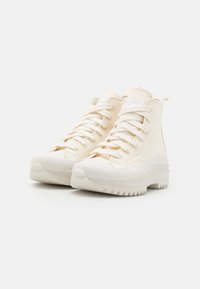 Höga sneakers i off-white tyg med strukturerat mönster, med vita snören och en kraftig gummisula med tandade kanter.