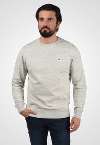 Sudadera gris de textura con cuello redondo, puños y bajo acanalados. Presenta un pequeño logo triangular en el lado izquierdo del pecho.