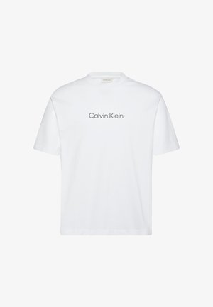 Bílé bavlněné tričko s krátkými rukávy. Má kulatý výstřih a potisk loga „Calvin Klein“ v šedé barvě přes hrudník.