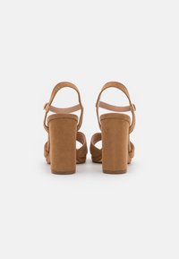 Tan suede block-heeled sandals with open backs, round toes, and adjustable ankle straps. Features a smooth, slightly textured surface.