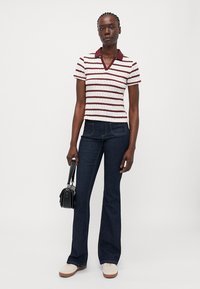 Kortermet stripet skjorte med dyp V-hals i kremfarge og burgunder, kombinert med mørkeblå flagrende jeans og hvite sko, bærende en liten veske.