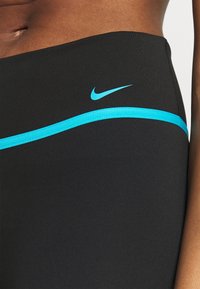 Musta urheiluhousut, joissa on sileä pinta, sininen kaareva koristelu ja Nike-logo vyötäröllä.