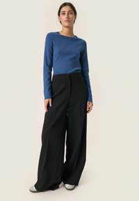 Blaues Langarmoberteil mit Rundhalsausschnitt, kombiniert mit hochtaillierten, weiten schwarzen Hosen. Glattes Material mit strukturiertem Sitz.