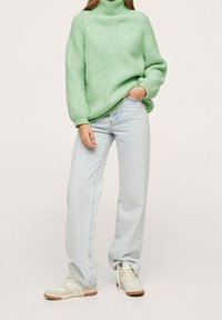 Pull à col roulé en maille épaisse vert menthe, coupe décontractée, associé à un jean pattes d'éléphant délavé clair et des baskets beiges avec des semelles marron.