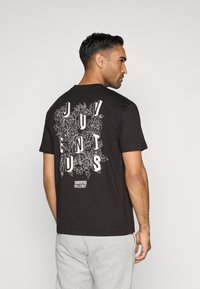 T-shirt de algodão preto com design floral e texto branco nas costas, mangas curtas e decote redondo.