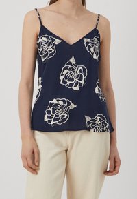 Námořnický bezramenný top s v-výstřihem, zdobený bílými květinovými vzory. Měkko působící látka, volný střih, nastavitelná ramínka a uvolněný fit.