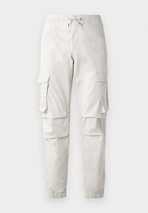 Light beige cargo pants with an elastic waistband, drawstring, side pockets, and tapered cuffs. Made from a smooth, lightweight fabric.