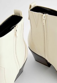 Krämfärgade läderankelboots med siddragkedjor, med spetsig tå och avsmalnande svart blockklack. Diskreta sömnadsdetaljer framhäver designen.