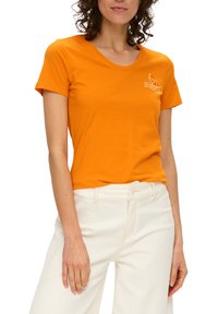 T-shirt à manches courtes de couleur orange, en coton, avec un col rond et un petit motif graphique blanc sur la poitrine.