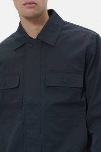 Chaqueta azul marino hecha de un tejido suave y ligero, con grandes bolsillos en el pecho y un cuello puntiagudo con botones de presión.