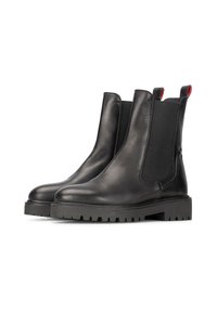 Botas Chelsea negras de cuero con paneles elásticos a los lados y tiradores rojos. Suela de goma gruesa con textura para agarre. Acabado suave.