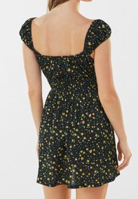 Schwarzes Blumenkleid mit gelben und grünen Mustern, ausgestattet mit einem gerafften Taillenbund und Puffärmeln. Leichtes, lässiges Design, geeignet für warmes Wetter.