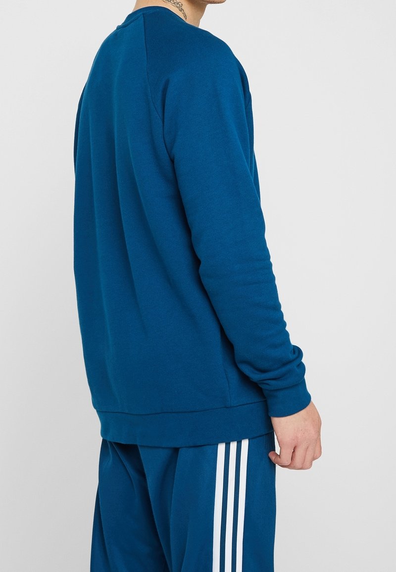 Sweatshirt bleu à manches longues, en tissu doux, avec un col rond et une coupe décontractée, associé à un pantalon bleu assorti avec des rayures blanches.
