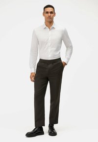 Witte button-up shirt gecombineerd met donkergrijze sneakers met elastische tailleband en zwarte veterschoenen. Glad stof en getailleerde pasvorm.