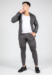 Mørkegrå zip-up hoodie med teksturerede skulderdetaljer, parret med matchende tapered joggers med ribbede detaljer og lommer, båret med sorte sneakers.