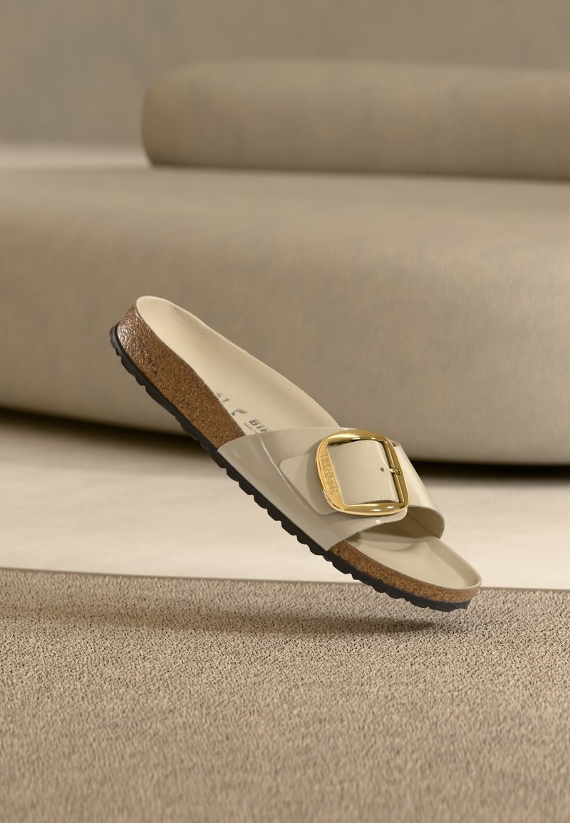 Μπεζ σανδάλι χωρίς λουράκια με γυαλιστερό λουράκι και μεγάλο χρυσό αγκράφα, με υφή καφέ κ αι μαύρης σόλας. Μινιμαλιστικός σχεδιασμός χωρίς σχέδια.