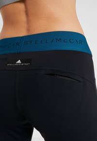 Czarne legginsy sportowe z turkusowym pasem, na którym widnieje logo "STELLA McCARTNEY". Posiadają małą zapinaną na zamek kieszeń z tyłu.