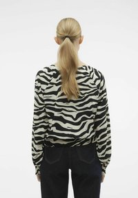Blusa a righe zebrate in bianco e nero con maniche lunghe, polsini elasticizzati e vestibilità morbida, abbinata a jeans in denim scuro.