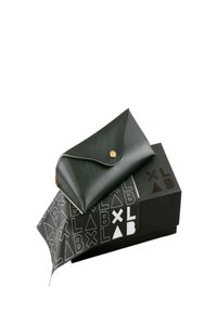 Svart läderpung med ett guldknäppstängning, som vilar på en svart låda med vita geometriska mönster och en mikrofiberputsduk.