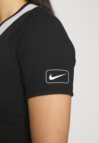 Musta, tiukkapitoinen urheilupaita lyhyillä hihoilla. Varustettu valkoisella Nike-logolla vasemmassa hihassa ja erottuvalla kaula-aukkosuunnittelulla.