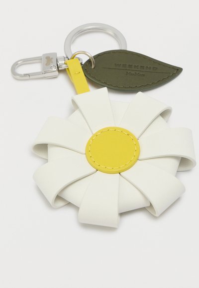 Μπρελόκ με μεταλλικό κλιπ, λευκά πέταλα λουλουδιού από δέρμα, κίτρινο κέντρο λουλουδιού από δέρμα και προσαρτημένη πράσινη ετικέτα φύλλου από δέρμα με κείμενο.