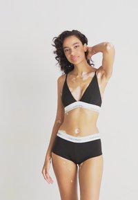 Bralette noire avec des fines bretelles et boyshorts noirs assortis. Présente une bande élastique blanche avec le logo "Calvin Klein". Texture de tissu lisse.