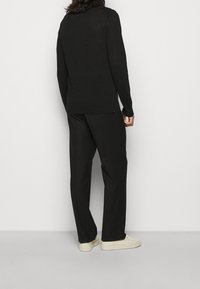 Czarna bluza z długimi rękawami i luźnym krojem, zestawiona z szerokimi czarnymi spodniami i kremowymi trampkami. Prosty, minimalistyczny design.